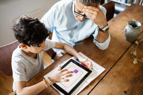 Blick von oben auf einen Jungen, der ein digitales Tablet benutzt, während er mit seinem Vater zu Hause sitzt - MASF03054