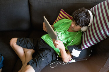 High angle view of boy listening music through digital tablet while reclining on sofa at home - MASF03055