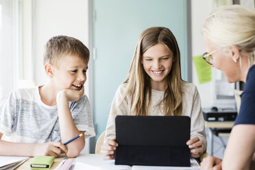 Happy girl using digital tablet while teacher and boy looking in classroom at school - MASF03058