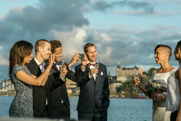 Glücklicher Mann steht mit Freunden beim Fotografieren eines lesbischen Paares auf einer Hochzeit - MASF03060