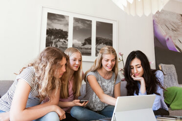 Glückliche Mädchen im Teenageralter benutzen einen Laptop, während sie zu Hause auf dem Sofa sitzen - MASF03063