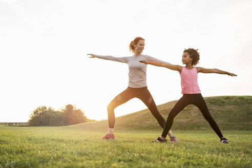 Happy mother looking at daughter exercising on grass against sky - MASF03066