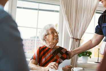 Glückliche ältere Frau sieht den Hausmeister an, während sie mit ihrer Familie Karten spielt - MASF03075