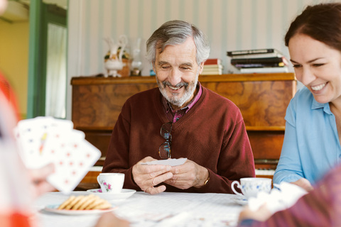 Glücklicher älterer Mann spielt Karten mit seiner Familie zu Hause, lizenzfreies Stockfoto