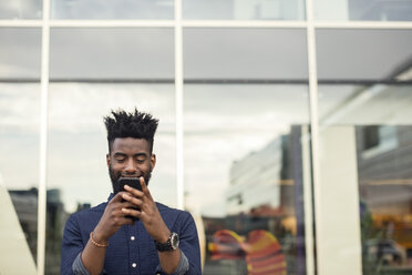 Happy young man using mobile phone against window - MASF03078