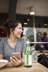 Happy woman wearing headphones resting at sidewalk cafe - MASF03083