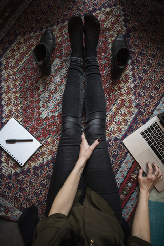 Niedriger Ausschnitt eines Bloggers, der einen Laptop benutzt, während er auf einem Teppich sitzt, lizenzfreies Stockfoto