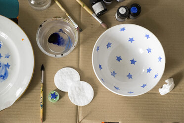 Overhead view of watercolor paints and brushes with bowls on cardboard - CAVF36473