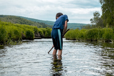 Rear view of boy fishing while standing in lake against cloudy sky - CAVF36488