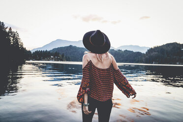 Rear view of woman if fedora hat looking at view while standing by lake during dusk - CAVF36496