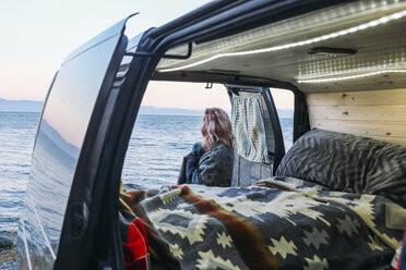 Rear view of woman looking at view while standing by open van - CAVF36507