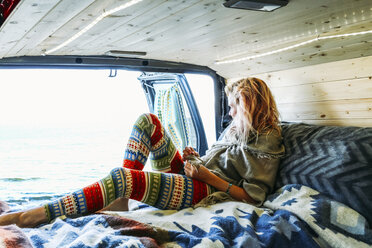 Frau schaut auf das Meer, während sie sich auf eine Matratze im Wohnwagen stützt - CAVF36529