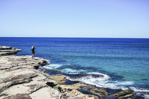 Rear view of woman standing on cliff against sea and clear sky - CAVF36552