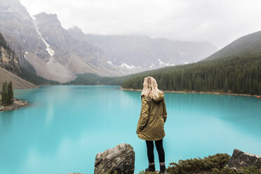 Rückansicht einer Wanderin mit Hand in der Tasche, die am Moraine Lake vor den Bergen im Banff National Park steht - CAVF36565