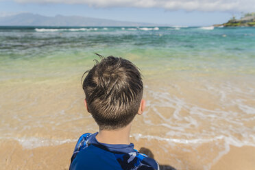 Rear view of boy standing at beach against sky during sunny day - CAVF36567