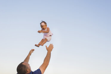 Low angle view of father throwing daughter into air against clear sky - CAVF36569