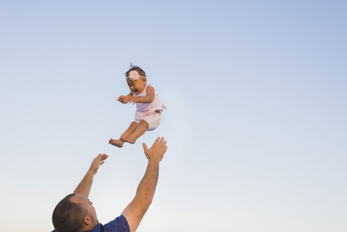 Niedriger Blickwinkel von Vater wirft Tochter in die Luft gegen klaren Himmel - CAVF36569