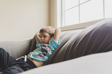 Thoughtful boy lying on sofa at home - CAVF36573