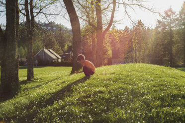Side view of boy crouching on grassy field during sunny day - CAVF36574
