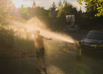 Verspielter Junge, der seinen Bruder mit Wasser bespritzt, während er am Auto steht - CAVF36579