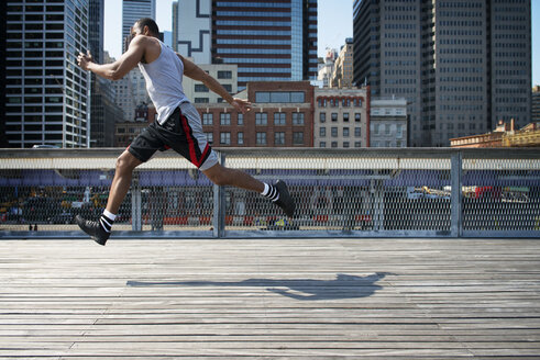 Side view of man jumping on boardwalk against modern buildings - CAVF36584