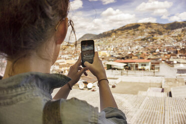 Rückansicht einer Frau, die ein Wohnviertel mit ihrem Smartphone gegen den Himmel fotografiert - CAVF36588