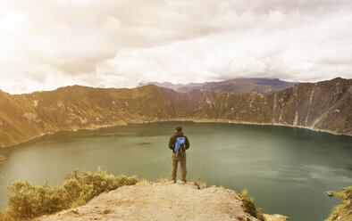 Man standing on cliff against Quilotoa and cloudy sky - CAVF36600