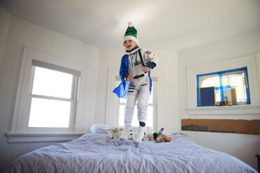 Glücklicher Junge trägt Kostüm und springt auf Bett zu Hause - CAVF36616