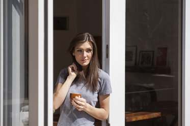 Beautiful woman holding coffee cup and standing at window - CAVF36627