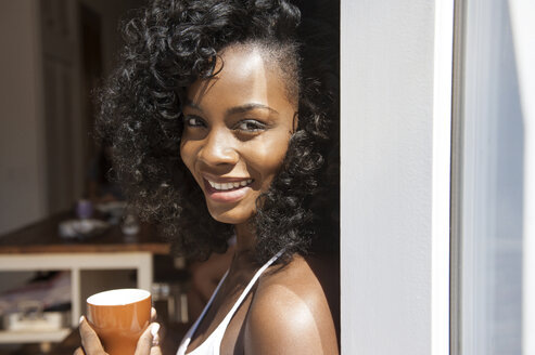 Porträt einer lächelnden Frau mit Kaffeetasse am Fenster - CAVF36635