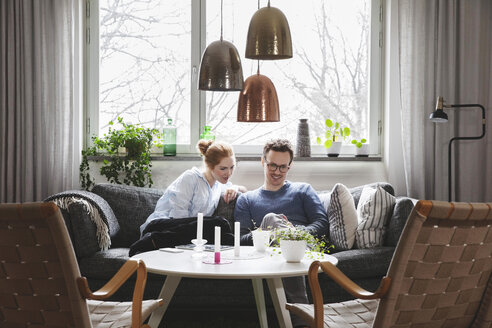 Ehepaar schaut in sein Smartphone, während es zu Hause auf dem Sofa sitzt - MASF03139