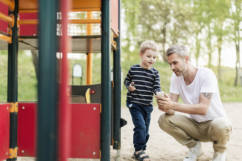 Vater zeigt seinem Sohn das Smartphone, während er sich auf dem Spielplatz vergnügt - MASF03169