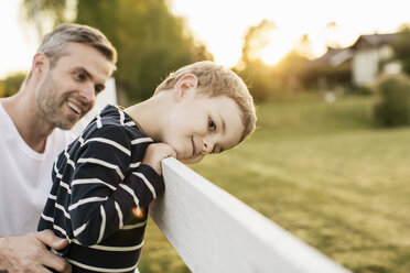 Vater sieht lächelnden Jungen an, der am Zaun einer Wiese lehnt - MASF03170