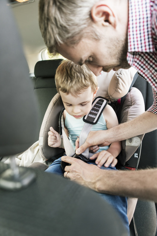 Vater befestigt Sicherheitsgurt für Sohn im Auto, lizenzfreies Stockfoto