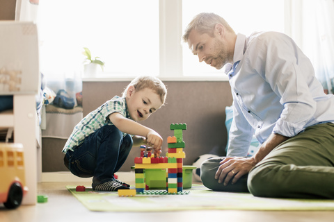 Vater und Sohn spielen mit Bauklötzen, während sie zu Hause sitzen, lizenzfreies Stockfoto