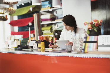 Eine Frau benutzt ein digitales Tablet und schreibt auf einem Notizblock an der Kasse in einem Geschäft - MASF03193