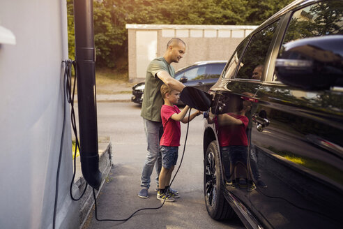 Father and son charging electric car by house - MASF03194