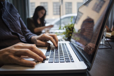 Nahaufnahme eines Geschäftsmannes, der einen Laptop benutzt, während ein Kollege am Tisch im Büro sitzt - MASF03196