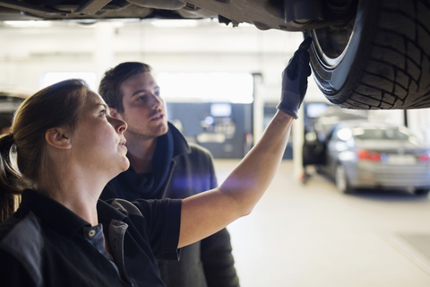 Nahaufnahme eines Mechanikers, der dem Kunden ein Rad unter dem Auto in der Werkstatt zeigt, lizenzfreies Stockfoto