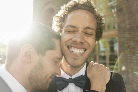 Nahaufnahme eines schwulen Mannes, der seinen fröhlichen, frisch verheirateten Partner mit geschlossenen Augen umarmt, lizenzfreies Stockfoto