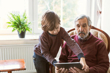 Boy assisting great grandfather in using digital tablet at home - MASF03228
