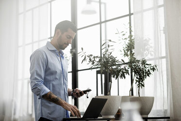 Geschäftsmann, der Technologie verwendet, während er am Tisch im Büro steht - MASF03232