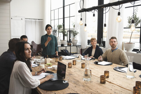 Geschäftsfrau erklärt ihren Kollegen während einer Besprechung am Tisch im Büro - MASF03238