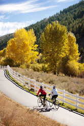 Friends riding bicycle on mountain road against sky - CAVF36652