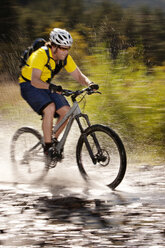 Hiker splashing water while riding bicycle in puddle - CAVF36653