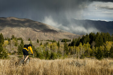 Rückansicht eines Mannes, der auf einer Wiese gegen Gewitterwolken Fahrrad fährt - CAVF36675