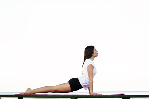 Seitenansicht einer Frau, die auf einer Gymnastikmatte trainiert, Meer gegen klaren Himmel - CAVF36729