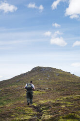 Rear view of man with backpack walking on mountain against sky - CAVF36747