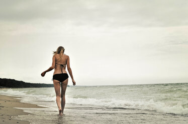 Rear view of woman wearing bikini walking at beach against clear sky stock  photo