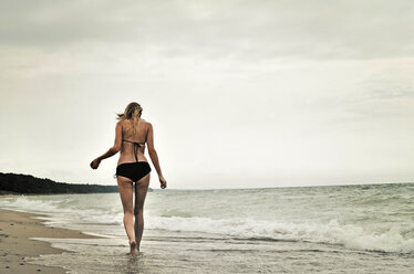 Rückansicht einer Frau im Bikini, die am Strand gegen den klaren Himmel läuft - CAVF36977